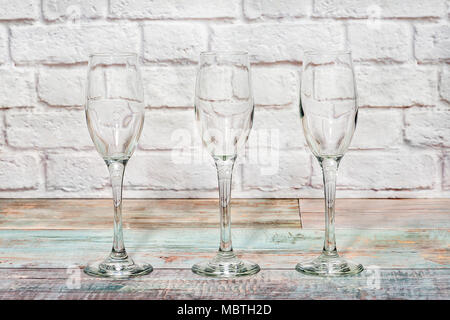 Three empty glass goblets on a rustic table with white bricks on background Stock Photo