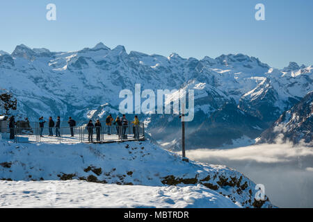 STOOS, SWITZERLAND - JANUARY 2018 - Group of tourists and skiers looking at beautiful snowy Alps from observing platform from top of Fronalpstock near Stock Photo