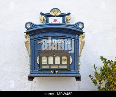 Glücksburg, Germany - April 8th, 2018 - Vintage German mailbox mounted on a whitewashed wall beside a green bush Stock Photo