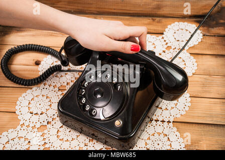 Girl hand holding old telephone headset on lace tablecloths and wooden background Stock Photo