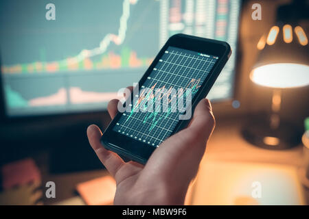 Male hand holding smartphone with online mobile app showing financial graph on display screen, trader investor using phone application for stock tradi Stock Photo