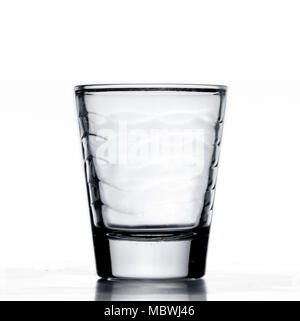 Small glass alcohol shot cup, being filled with blue water, or liquid, closeup, white background with reflection Stock Photo