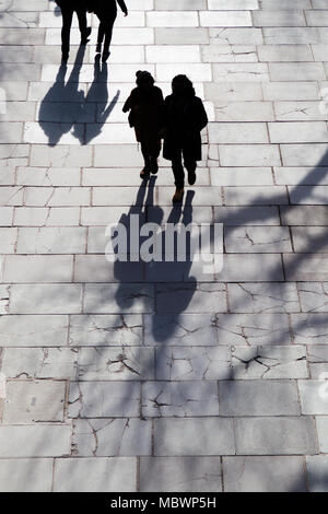 Silhouettes and shadows of people walking near the Festival Pier and Royal Festival Hall on the south bank of the Thames, seen from Waterloo Bridge. Stock Photo