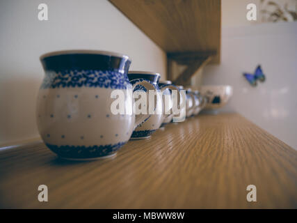 Row of thick traditionally ornamented white and blue mugs standing on the wooden shelf. Stock Photo