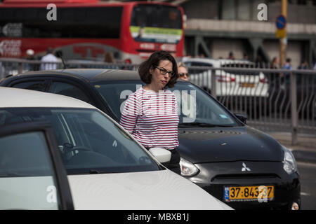 Tel Aviv, Israel. 12th April, 2018. A woman stands next to her vehicle on a highway and observes two minutes of silence to mark the Yom HaShoah (Holocaust and Heroism Remembrance Day), which commemorates approximately six million Jews who perished in the Holocaust that was carried out by Nazis, in Tel Aviv, Israel, 12 April 2018. Yom HaShoah is an annual occasion on which an air raid siren sounds throughout the whole country. While almost everything comes to a complete halt, Israelis are expected to observe two minutes of solemn reflection while the siren is sounded. Credit: dpa picture allian Stock Photo