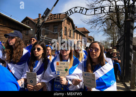 Oswiecim, Poland. 12th Apr, 2018. Participants wave Israeli flags while holding placards at the main gate of the former Nazi German Auschwitz-Birkenau death camp during the 'March of the Living' at Oswiecim. The annual march honours Holocaust victims at the former Nazi German Auschwitz-Birkenau death camp in southern Poland. Credit: Omar Marques/SOPA Images/ZUMA Wire/Alamy Live News Stock Photo