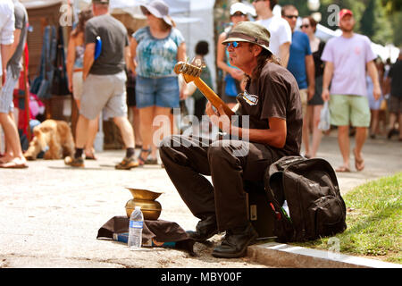 Atlanta, GA, USA - August 16, 2014:  A man plays bass guitar for tips while sitting on the curb at the Piedmont Park Arts Festival. Stock Photo