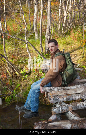 Tourist sits on a bridge over creek in autumn forest Stock Photo