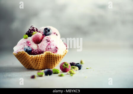 Pink ice cream with berries, strawberries, blueberries, raspberries, pistachios in waffle basket. Summer food concept, copy space. Healthy gluten free fruit ice-cream Stock Photo