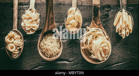 Different  pasta types  in wooden spoons on the table. Stock Photo