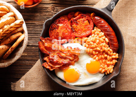 English Breakfast with sausages, grilled tomatoes, egg, bacon, beans and bread on frying pan. Stock Photo