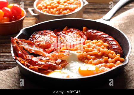 English Breakfast with sausages, grilled tomatoes, egg, bacon and beans on frying pan.