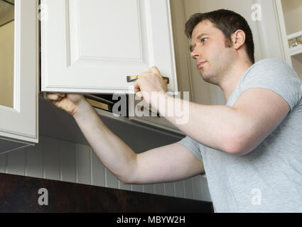 Professional handyman installing cabinet door in the kitchen. Stock Photo
