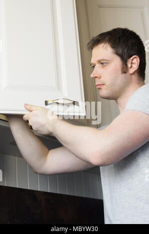 Professional handyman installing cabinet door in the kitchen. Stock Photo