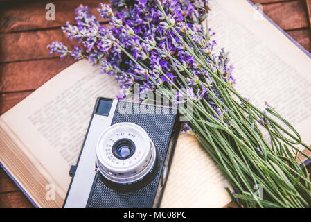 Freshly cutted lavender flowers and a vintage photo camera over an open book.Wooden background Stock Photo