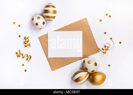 Easter festive decoration. Top view of easter eggs colored with golden paint in differen patterns and empty mock-up card in a kraft envelope. Various  Stock Photo