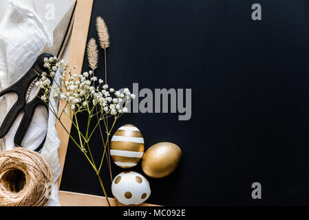 Easter background. Easter eggs in various golden designs, scissors, flowers and hemp ball over black story board. Copy space Stock Photo