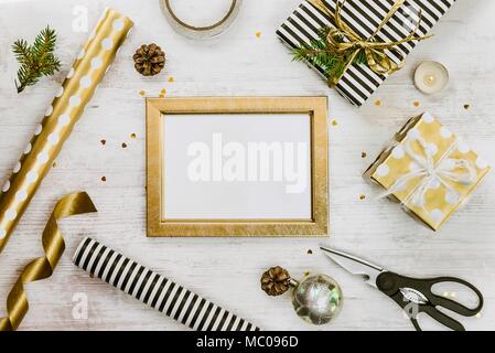 Golden ptoto frame, gift boxes, pine cones and christmas toys and wrapping materials on a white wood old background. Christmas concept. Frame mock up. Stock Photo