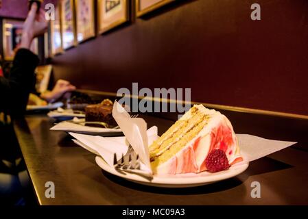 Close up of various slices of cakes served at a bar counter. People eating cakes in a cake shop. Stock Photo