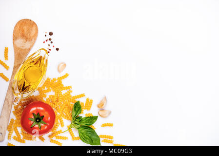 Top view of pasta ingredients over white background - raw fusilli, fresh basil, garlic cloves, olive oil and ripe tomatoe. Italian food concept. Copy  Stock Photo