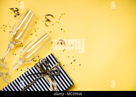 Celebration background - top view of two chrystal champagne glasses, a gift box wrapped in black and white striped paper, ribbons and star shaped gold Stock Photo