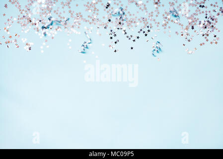 Star shaped silver sequins and silver ribbons over blue background. Copy space. Stock Photo