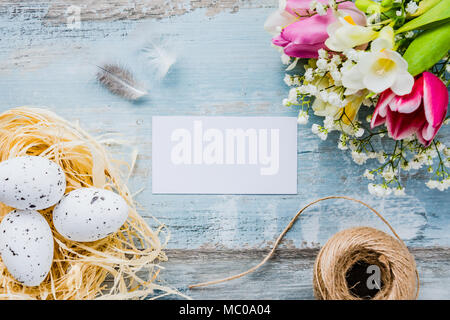Top view of Easter eggs in a nest. Spring flowers and feathers over blue rustic wood background. Empty card. Stock Photo