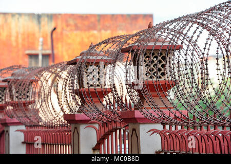 Security measures on the outside of a red brick building in Jaipur, India. Razor wire atop a red painted, ornamental wrought iron fence Stock Photo