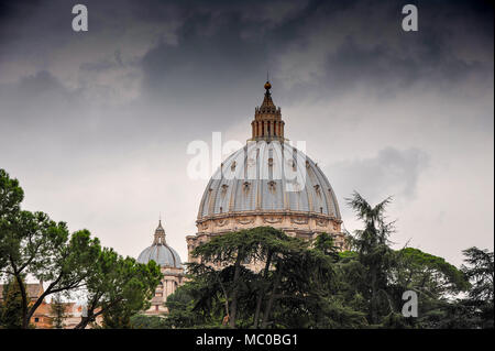 St. Peter's Basilica, Vatican City viewed through the treetops. Beautiful dome framed by dark green foliage against a dark, stormy sky Stock Photo