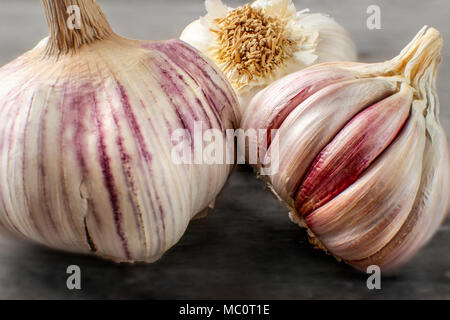 Detailed photo of garlic bulbs on wooden table, some purple cloves uncovered under garlic skin. Stock Photo