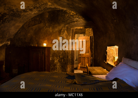 Cave-like medieval guest room with lit candles, massive wooden doors and an arched ceiling in Santo Stefano di Sextantio diffused hotel, Santo Stefano Stock Photo