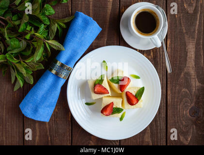 Delicate cottage cheese and creamy souffle in the form of cubes, decorating with mint leaves and fresh strawberries on a white plate Stock Photo