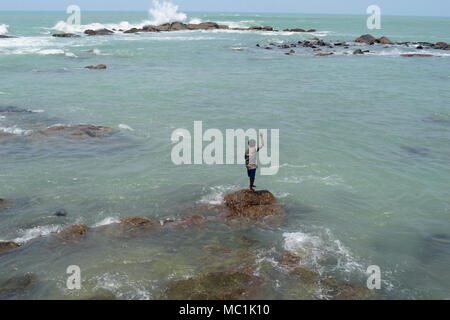 A fisherman standing on the rock and trying to catch fishes from the sea ,Kanyakumari ,India Stock Photo