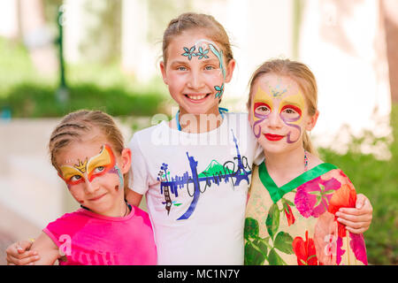 Happy little girls with face art paint in the park. Child's birthday masquerade party, friends having fun, laugh and hugging each other. Entertainment Stock Photo