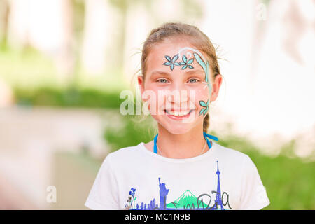 Happy little girl with face art paint in the park. Child's birthday masquerade party have fun, laugh. Entertainment and holidays. Stock Photo