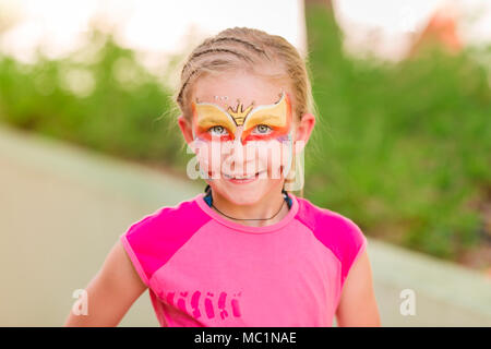 Happy little girl with face art paint in the park. Child's birthday masquerade party have fun, laugh. Entertainment and holidays. Stock Photo