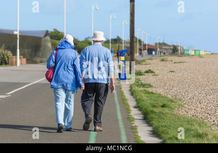 Senior couple walking away holding hands along the seafront promenade, on a sunny day in Littlehampton, West Sussex, England, UK. seafront stroll. Stock Photo