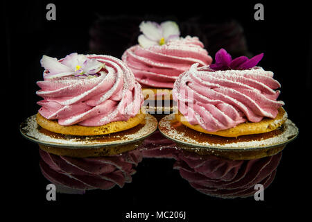three pink zephyr cookies decorated with violet and white flowers on black mirror background  with reflection Stock Photo