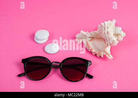 Sunglasses, white sea shells and pebbles on a pink background Stock Photo