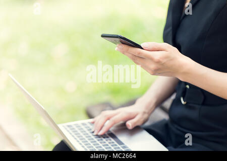 Business women using laptop and smartphone to working her job in the park outdoor Stock Photo