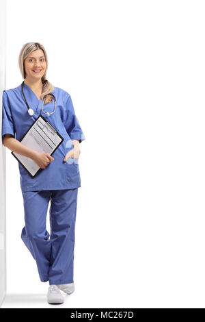 Full length portrait of a female doctor holding a clipboard and leaning against a wall isolated on white background Stock Photo