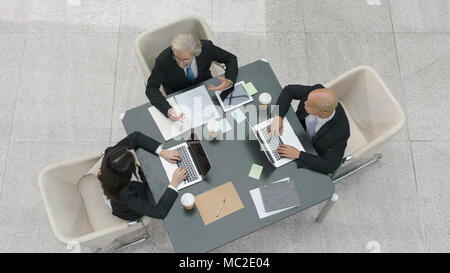 high angle view of three corporate executives meeting discussing business in modern office. Stock Photo
