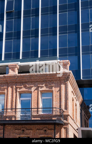 Small old brick house and standing right behind him modern building of glass and steel. Stock Photo