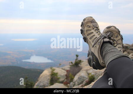 Hiking boots at the top of Mount Chocorua, in the White Mountains of New Hampshire. A view of lakes, fall foliage, and cloudy skies form the top. Stock Photo