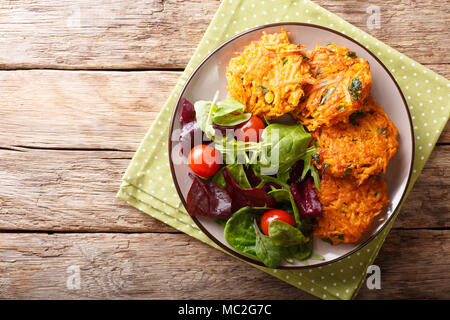 Homemade fritters of sweet potatoes and fresh mix of salad on a plate close-up. horizontal top view from above Stock Photo
