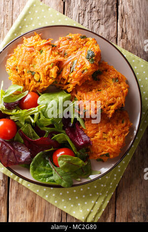 Fritters of sweet potatoes with greens and fresh salad on a plate close-up. Vertical top view from above Stock Photo