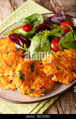 Fried pancakes from sweet potato and fresh mix salad on a plate close-up. vertical Stock Photo