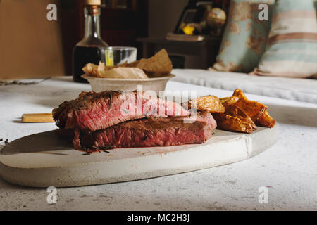 Barbecued steak on cutting board. Sealed with a strong, juicy and pink fire inside. with fried potato chips. Stock Photo