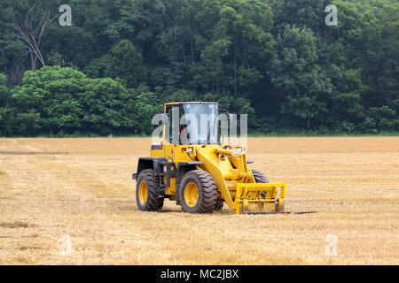 Yellow tractor sits idle in a golden field after harvest Stock Photo