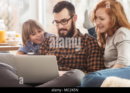 Happy family watching photos together on a laptop while sitting on a couch Stock Photo